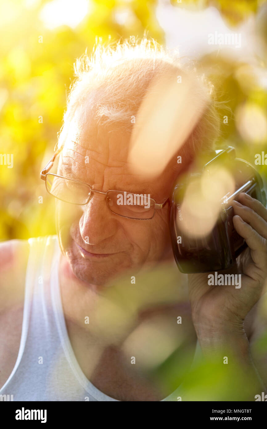 The old man standing outdoor and listen to a portable radio Stock Photo