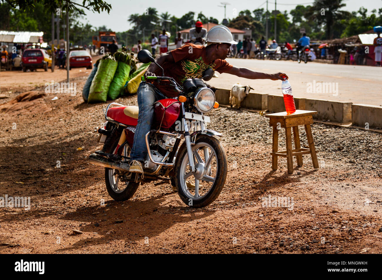 Yongoro, Sierra Leone - June 03, 2013: a bottle full of super petrol for refueling and an unknown man with a motorbike in the village in front of the  Stock Photo