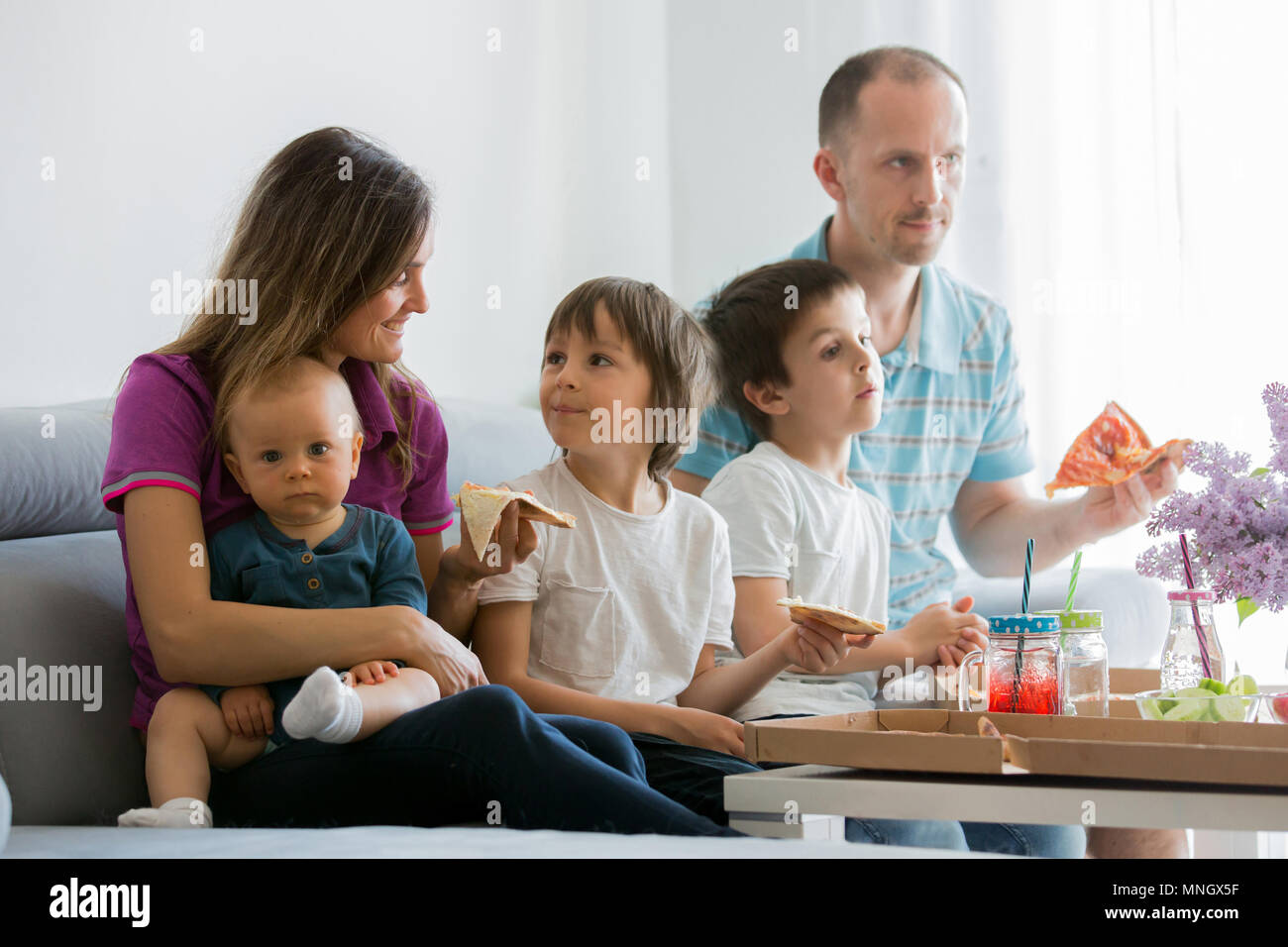 Beautiful young family with three children, eating pizza at home and watching TV on a sunday Stock Photo