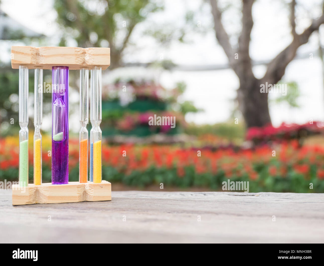 Hourglass on wooden table, blurred flower background, Stock Photo