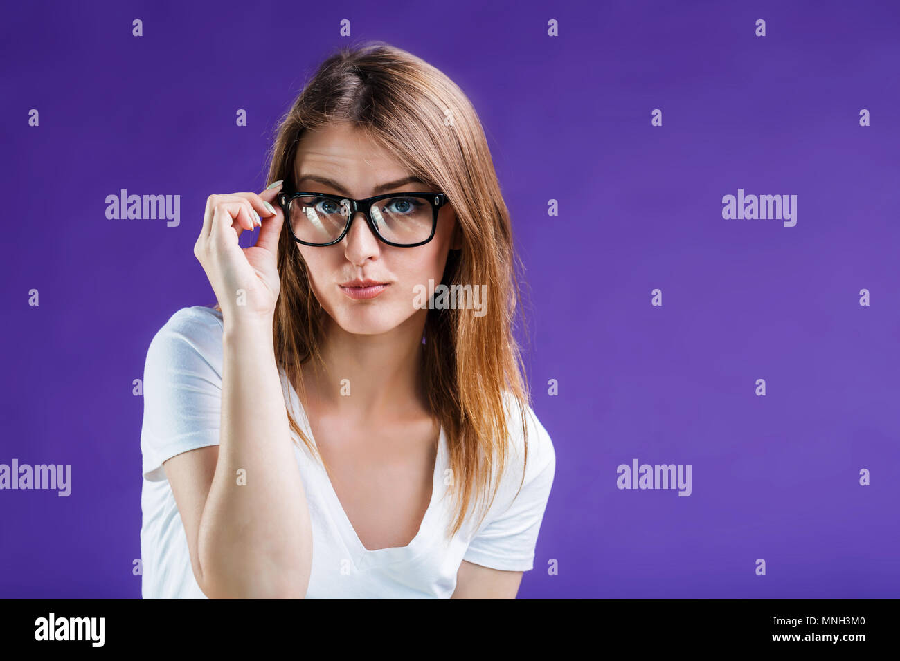 Portrait of pretty blonde woman dressed in white t-shirt and eyeglasses posing to camera, isolated on blue studio background Stock Photo