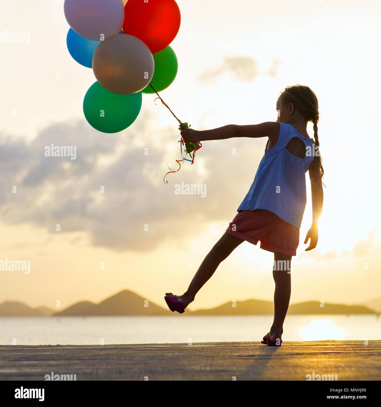 Silhouette of adorable happy little girl with bunch of balloons on sea
