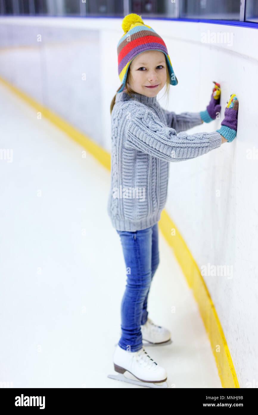 Adorable little girl wearing jeans, warm sweater and colorful hat skating on ice rink Stock