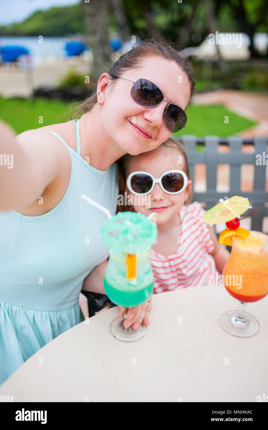 Happy mother and her adorable little daughter at outdoors cafe taking selfie while drinking tropical juice Stock Photo
