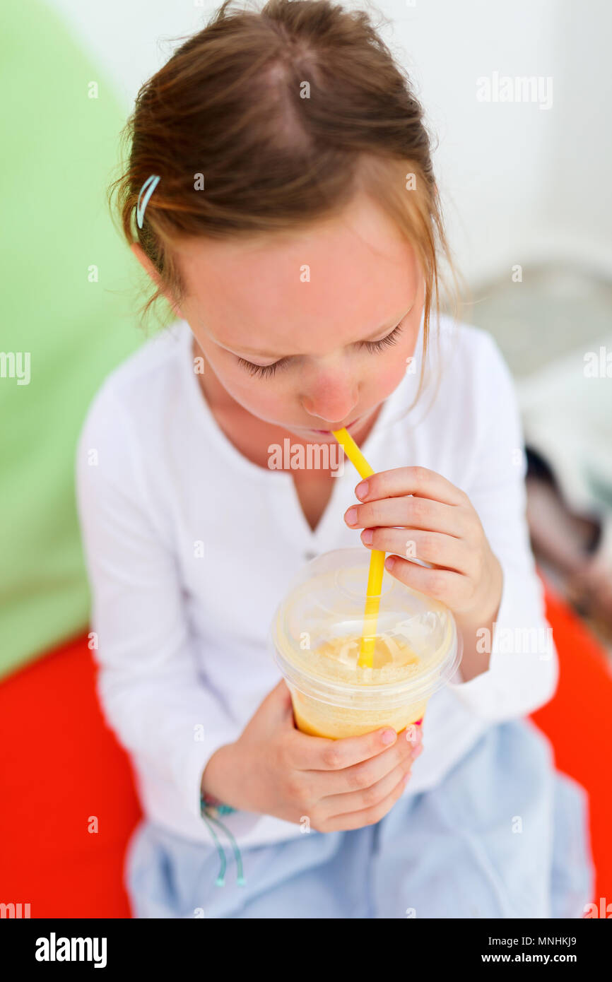 Adorable little girl drinking fresh smoothies on a colorful pillows at outdoor cafe on summer day Stock Photo