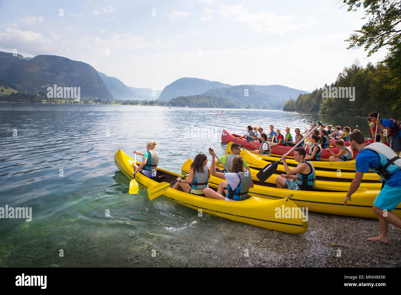 Young adults of school class are entering water of lake Bohinj with canoes, largest permanent lake located in Bohinj Valley of Julian Alps, Triglav National Park, Slovenia Stock Photo