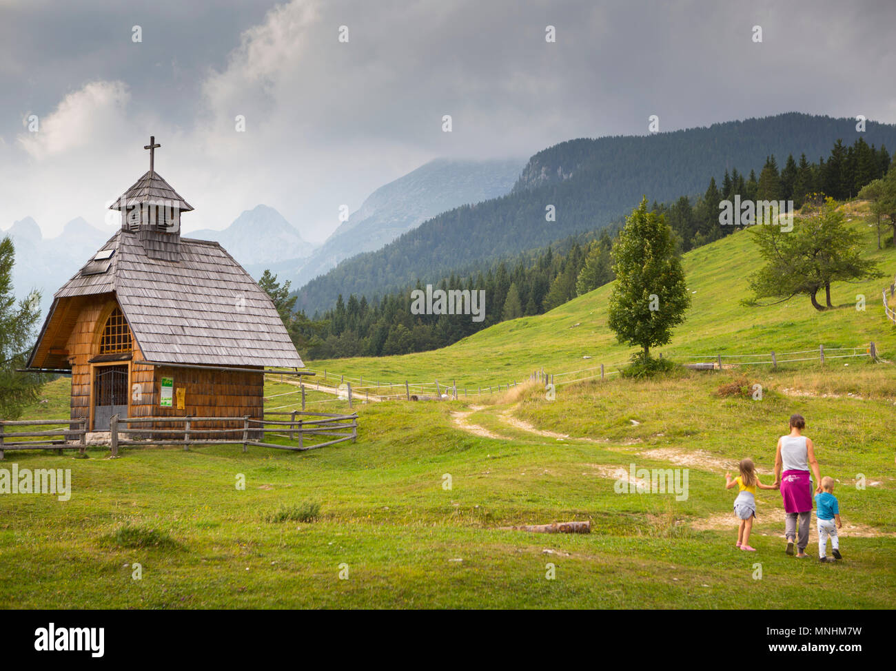 Woman and two children are hiking to chapel at Uskovnica alpine pasture at Pokljuka Plateau, Uskovnica, Triglav, Slovenia Stock Photo