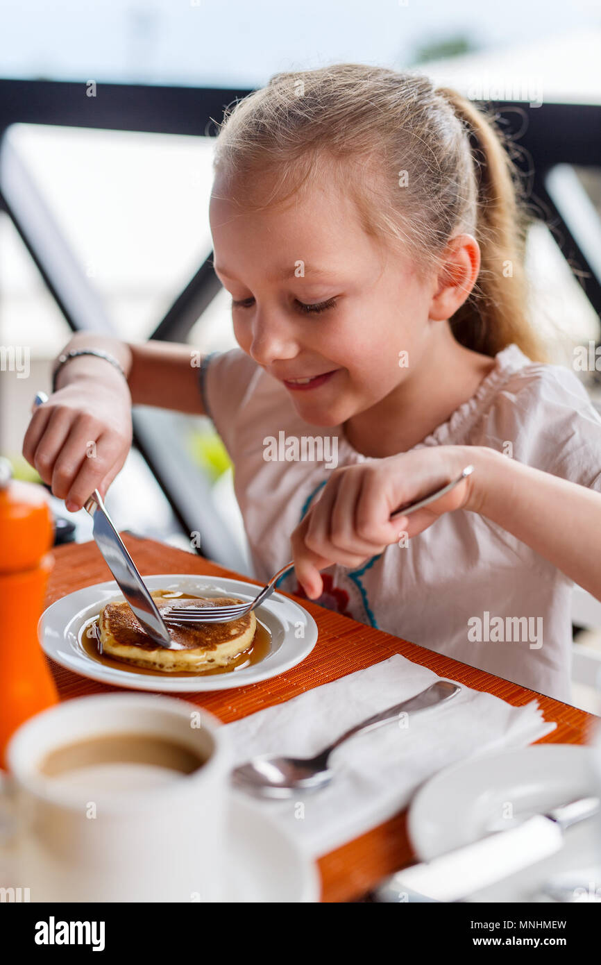 Adorable little girl eating pancake for breakfast in restaurant Stock
