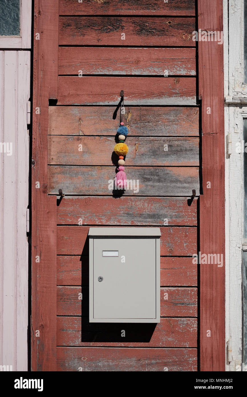 A blank mailbox and handmade fluffy windchime hanging on a wooden wall of an old abandoned house Stock Photo