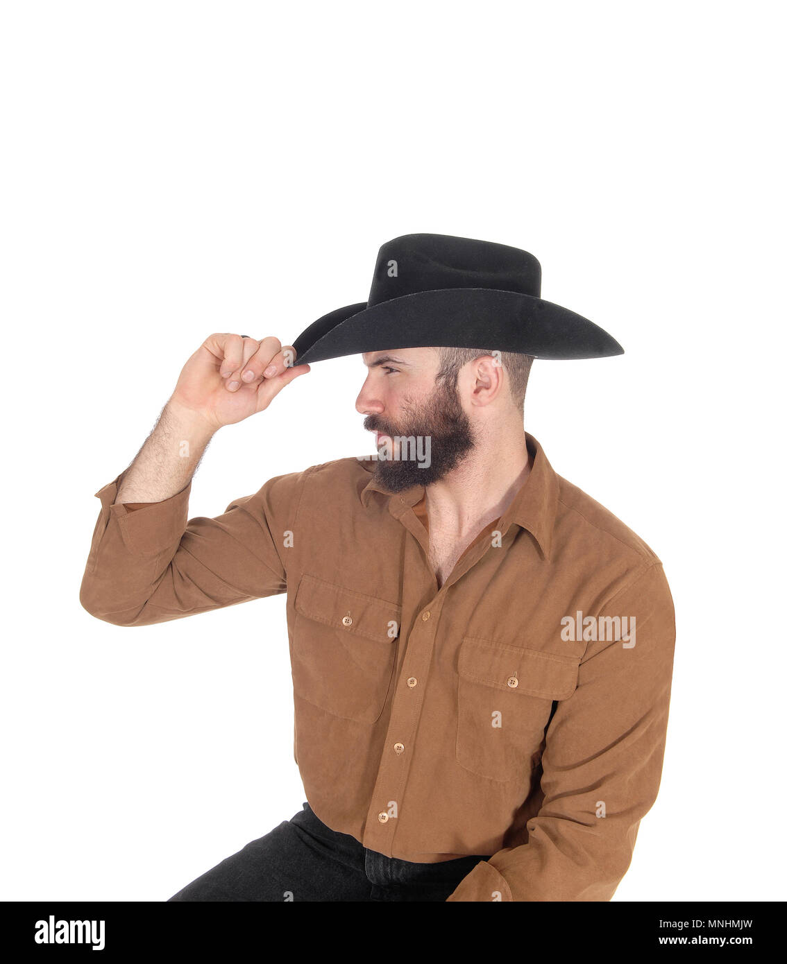 A young man sitting on a chair in profile wearing a black cowboy hat and looking away, isolated for white background Stock Photo