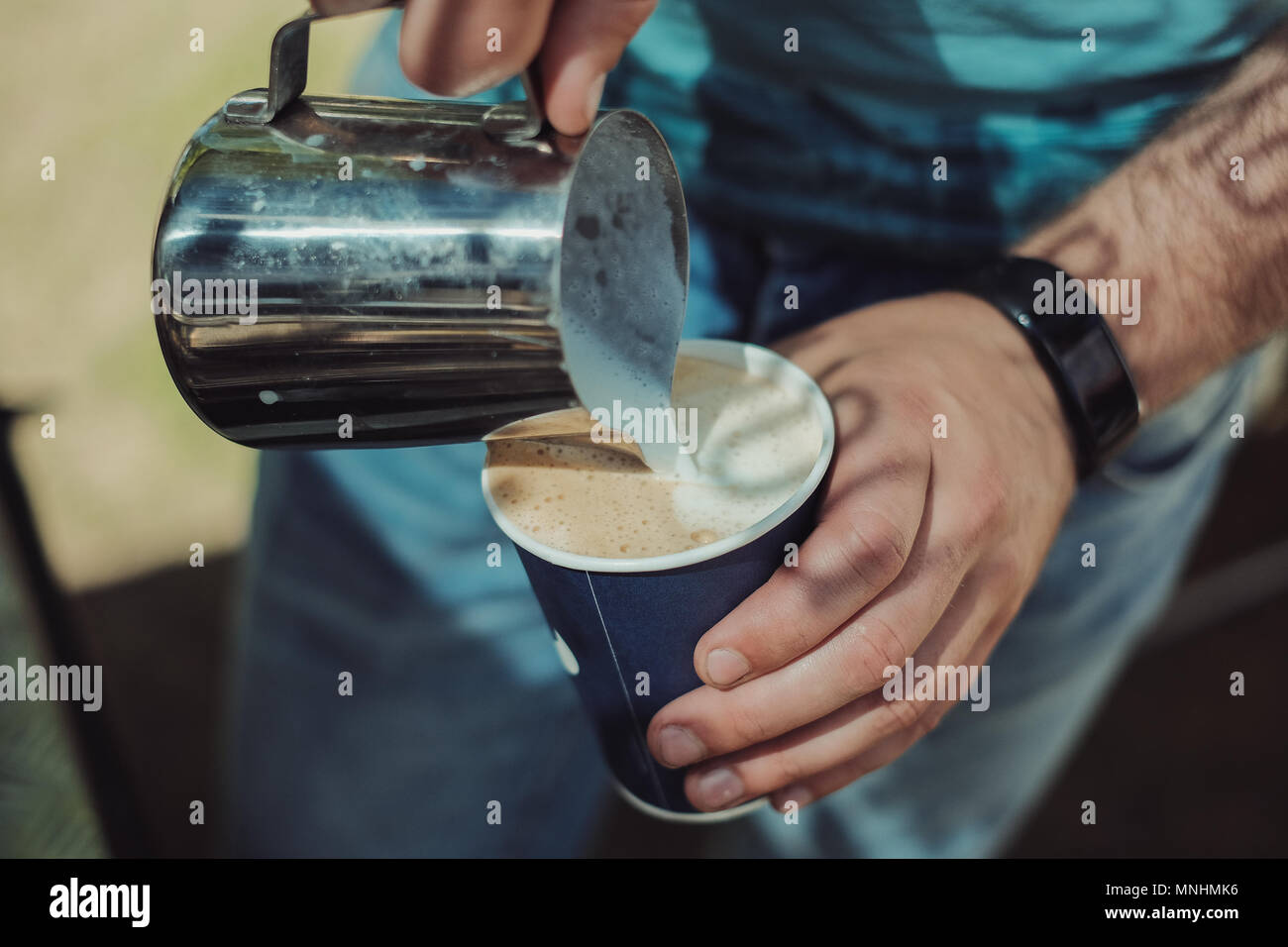 A barista pours steamed milk in a paper coffee cup to make a cappuccino. Old film look with shallow focus Stock Photo