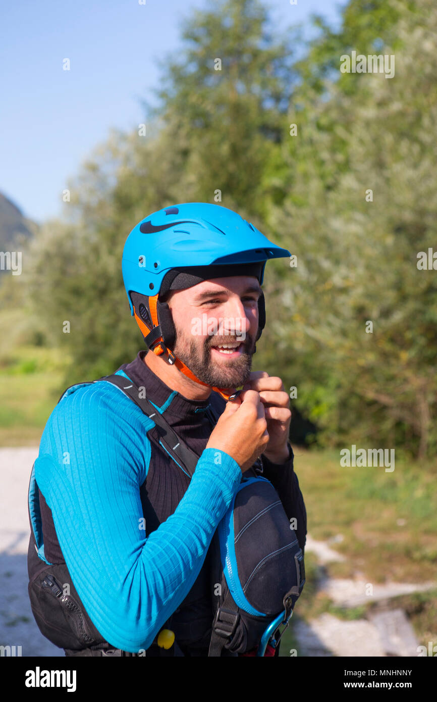 Smiling kayaker with beard putting on safety helmet before kayaking in Soca River near Bovec, Slovene Littoral, Slovenia Stock Photo