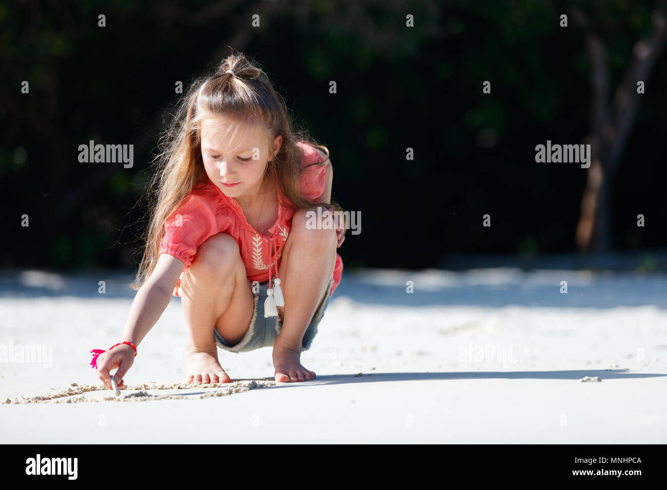 Little girl at tropical beach playing with sand Stock Photo. 