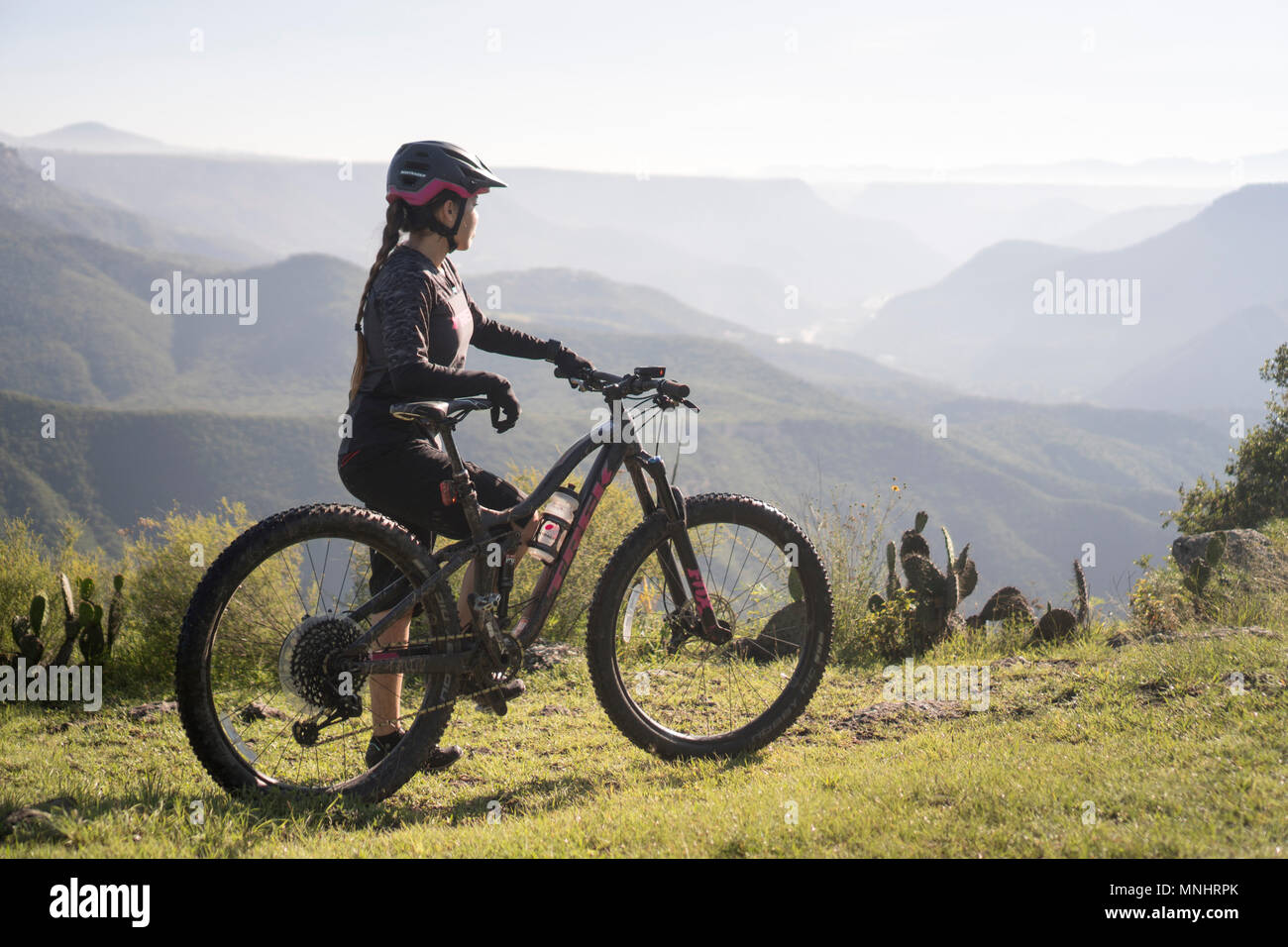 Side view of woman standing with mountain bike in natural setting with mountains in background, Pena del Aire, Huasca de Ocampo, Hidalgo, Mexico Stock Photo