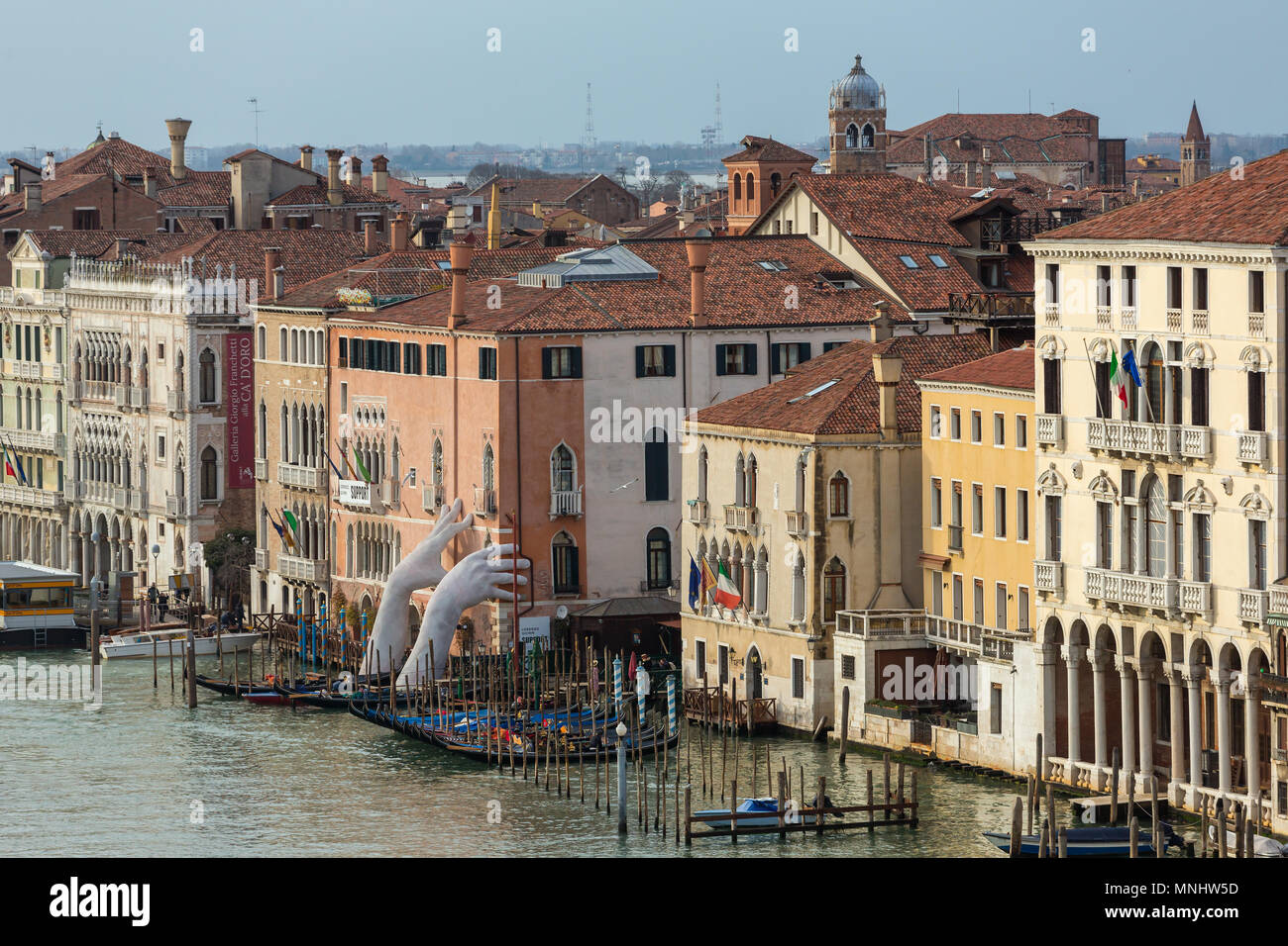 Venice, Italy - March 20, 2018: Giant hands rise from the water of Grand Canal to support the building in Venice. This powerful report on climate chan Stock Photo