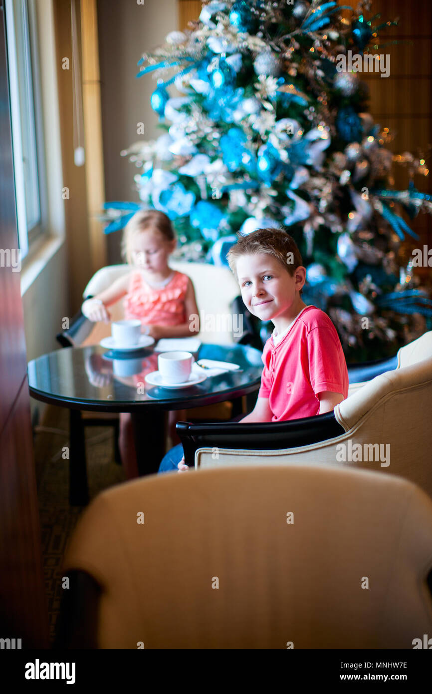 Two children drinking tea from white cups in a room decorated for Christmas Stock Photo
