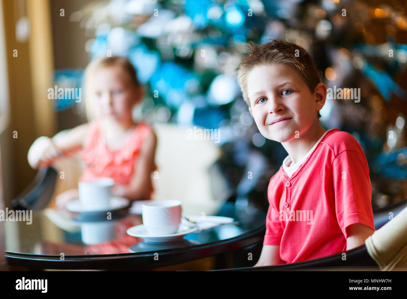 Two children drink tea from white cups in a room decorated for Christmas Stock Photo