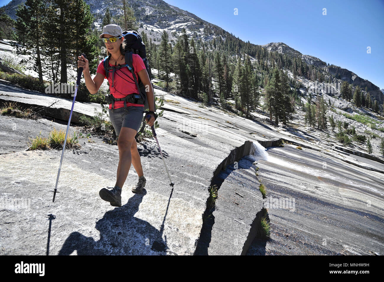 Backpacker hiking across a granite slab on the Bishop Pass Trail out of Dusy Basin into Le Conte Canyon on a two-week trek of the Sierra High Route in Kings Canyon National Park in California. The 200-mile route roughly parallels the popular John Muir Trail through the Sierra Nevada Range of California from Kings Canyon National Park to Yosemite National Park. Stock Photo