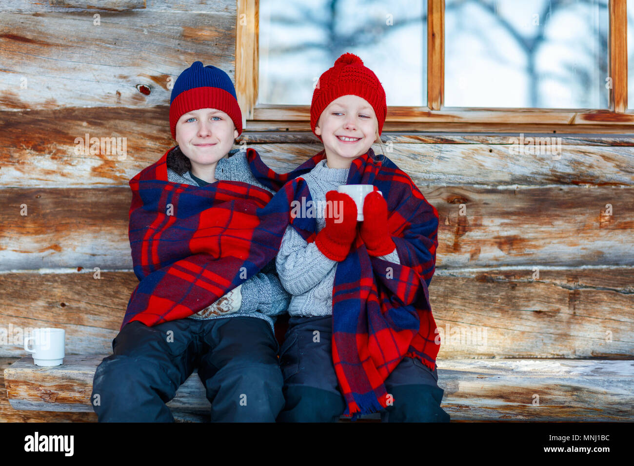 Kids outdoors on beautiful winter day drinking hot chocolate in front of log cabin vacation house Stock Photo