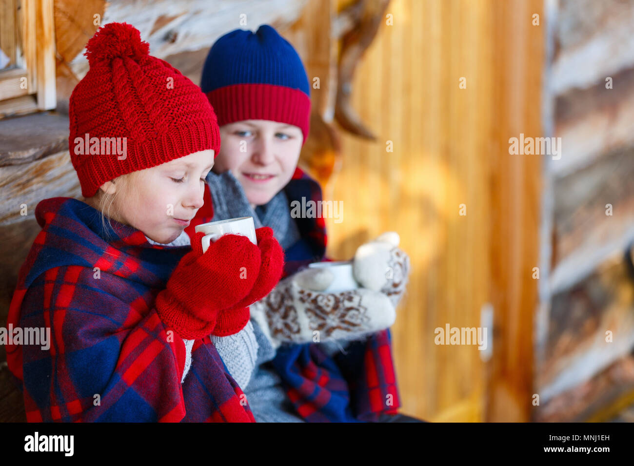 Kids outdoors on beautiful winter day drinking hot chocolate in front of log cabin vacation house Stock Photo