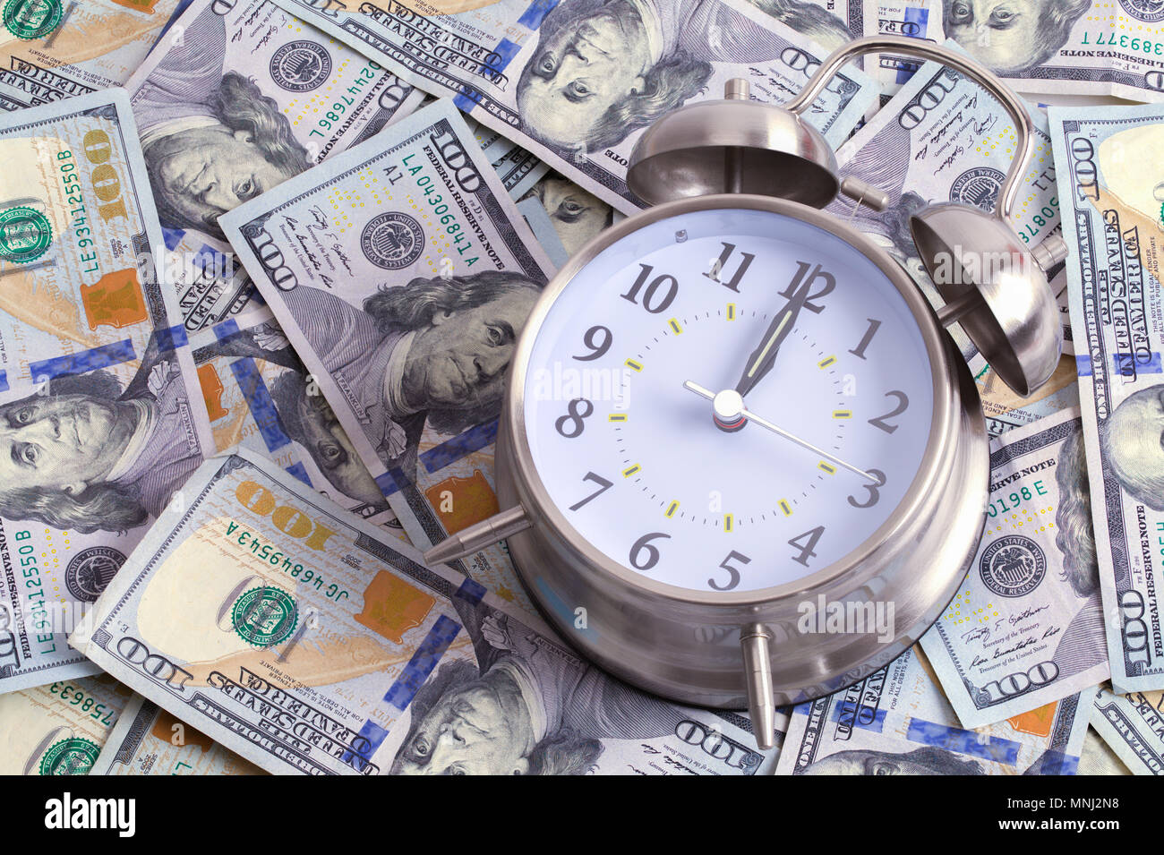 Clock on Top a Large Pile of Hundred Dollar Bills. Stock Photo