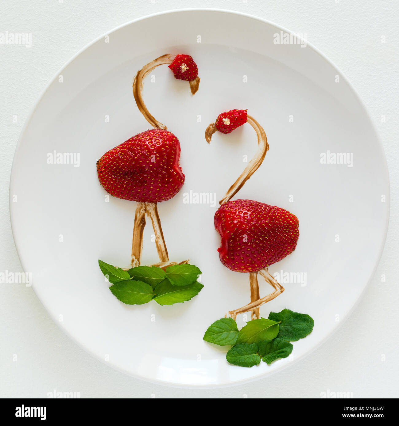 Food art creative concept. Flamingos on white plate. Strawberry, chocolate and mint composition. Top view. Stock Photo