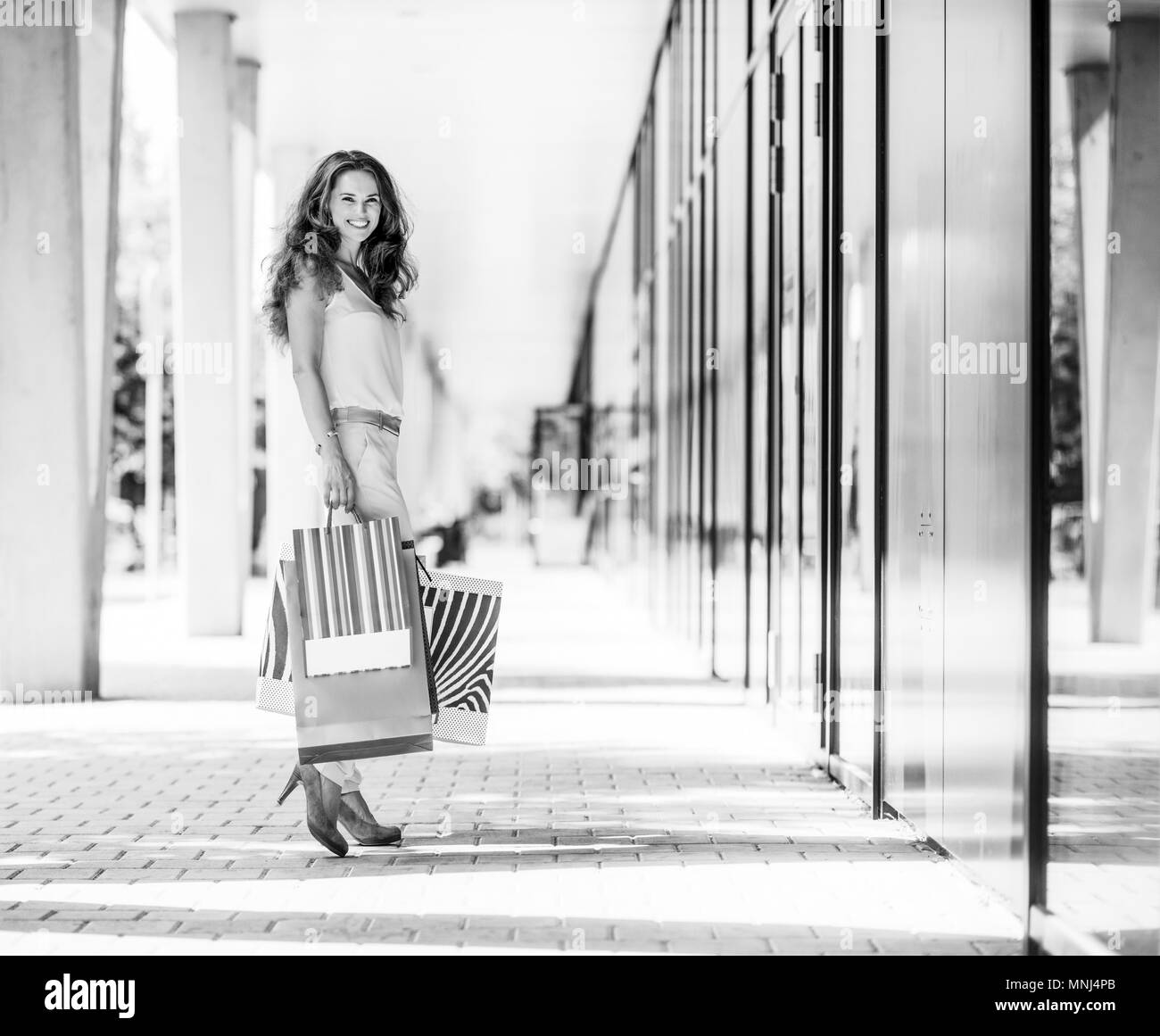 A brown-haired woman stops for a moment to look back a the viewer. She is clearly happy about her many purchases, all held in colourful shopping bags  Stock Photo