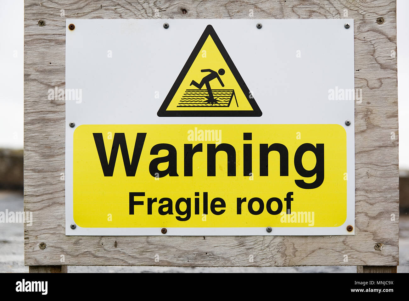 Warning fragile roof sign black text on yellow and white background with symbol of man stepping on and breaking roof Stock Photo