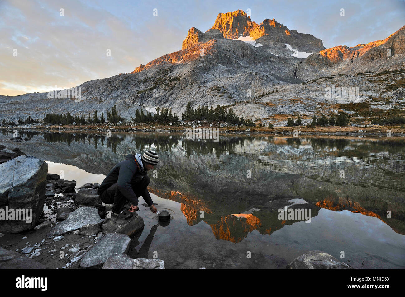 Backpacker dips water at camp near Thousand Island Lake with Banner Peak in background on a two-week trek of Sierra High Route in Minarets Wilderness, Inyo National Forest, California, USA Stock Photo