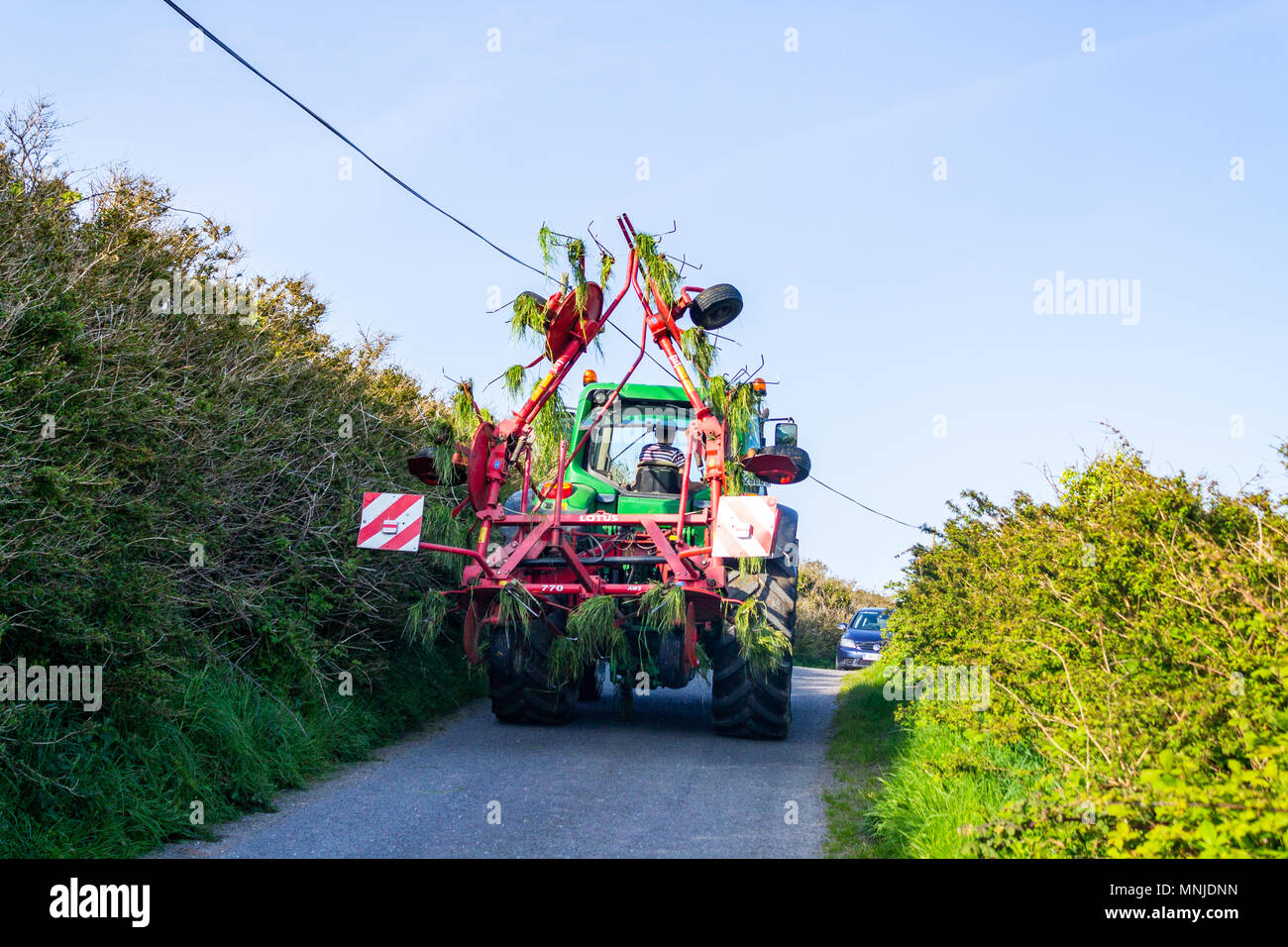 tractor with a set of spinners on the back driving up a country lane in ireland after turning over cut grass for silage. Stock Photo