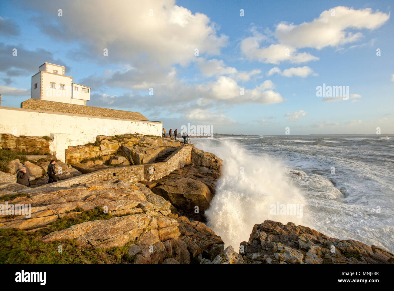 Group of people watching waves splashing on coastal rocks at dusk, Ploemeur, Morbihan, France Stock Photo
