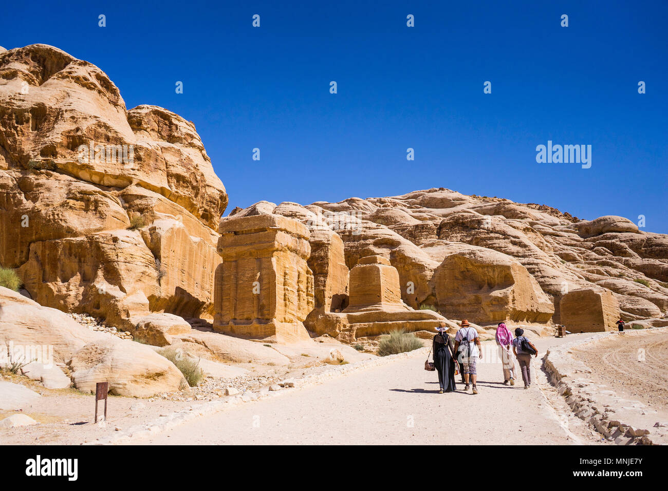 Tourists walking on footpath in Petra with tombs and temples carved in sandstone, Wadi Musa, Maan Governorate, Jordan Stock Photo