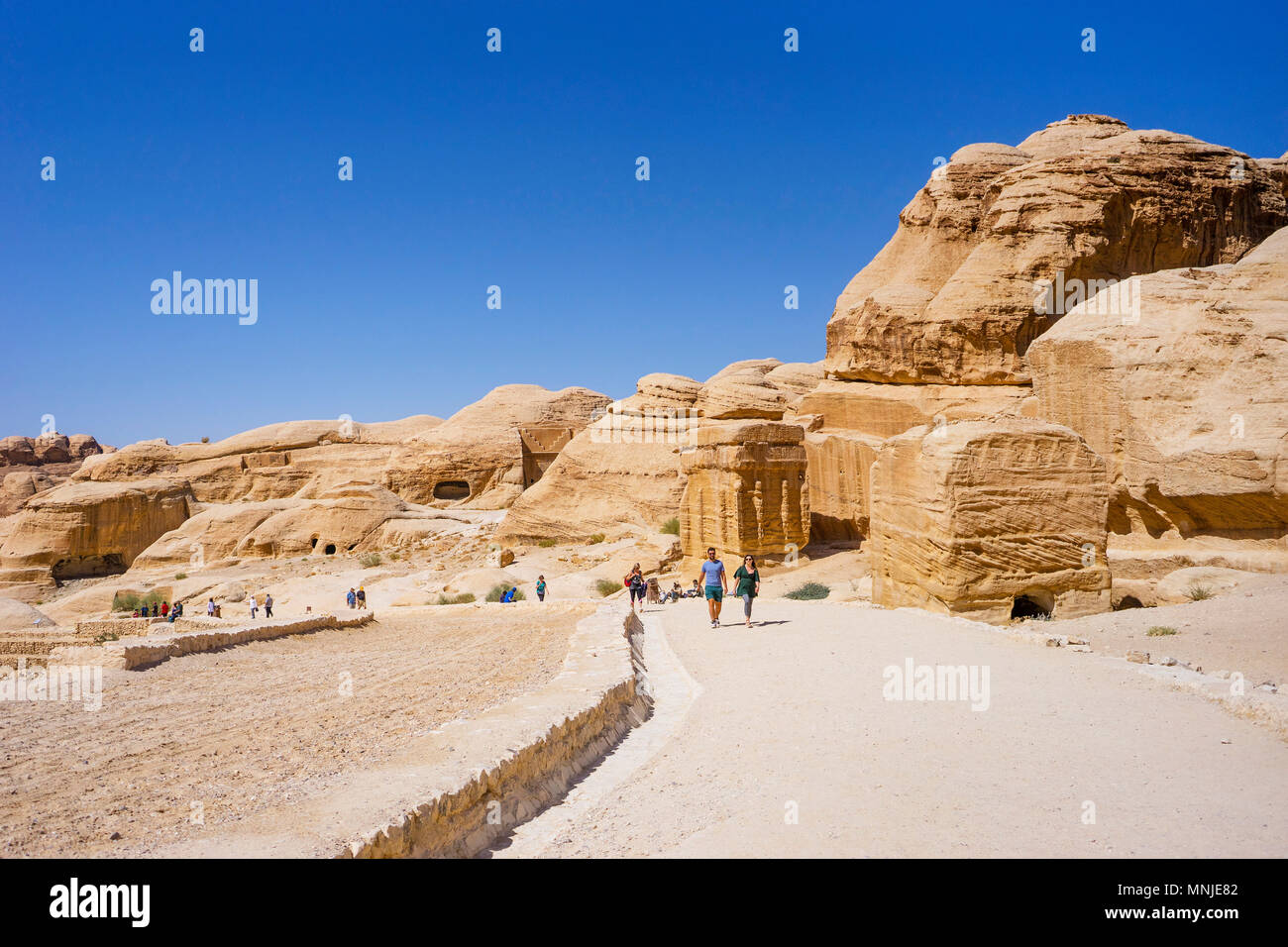 Tourists walking on footpath entering Petra from Visitors Center with tombs and temples carved in sandstone, Wadi Musa, Maan Governorate, Jordan Stock Photo