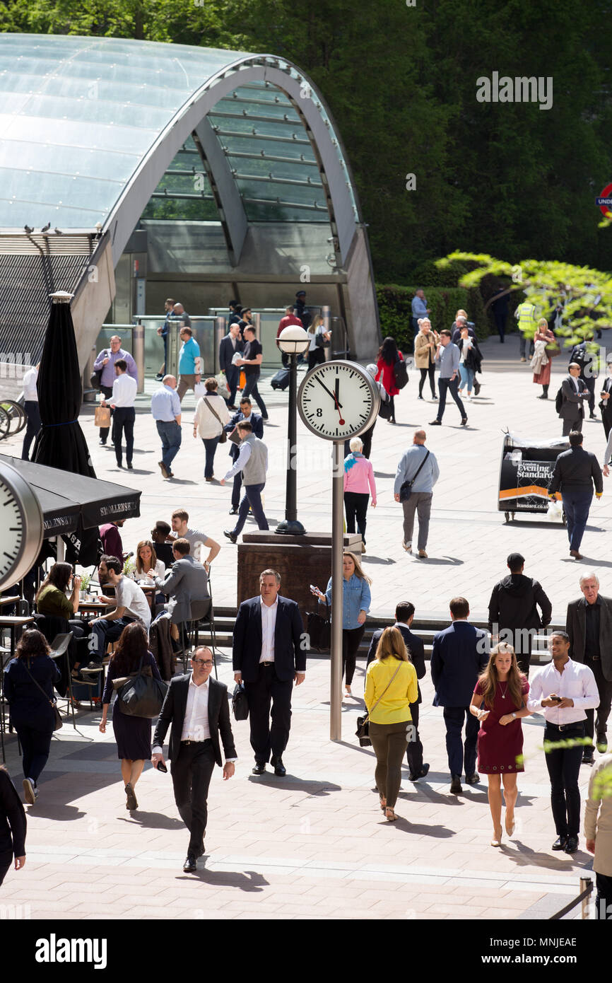 The glass arch entrance to Canary Wharf tube station, with professionals in the foreground heading to and from work, or on their lunch breaks. Stock Photo