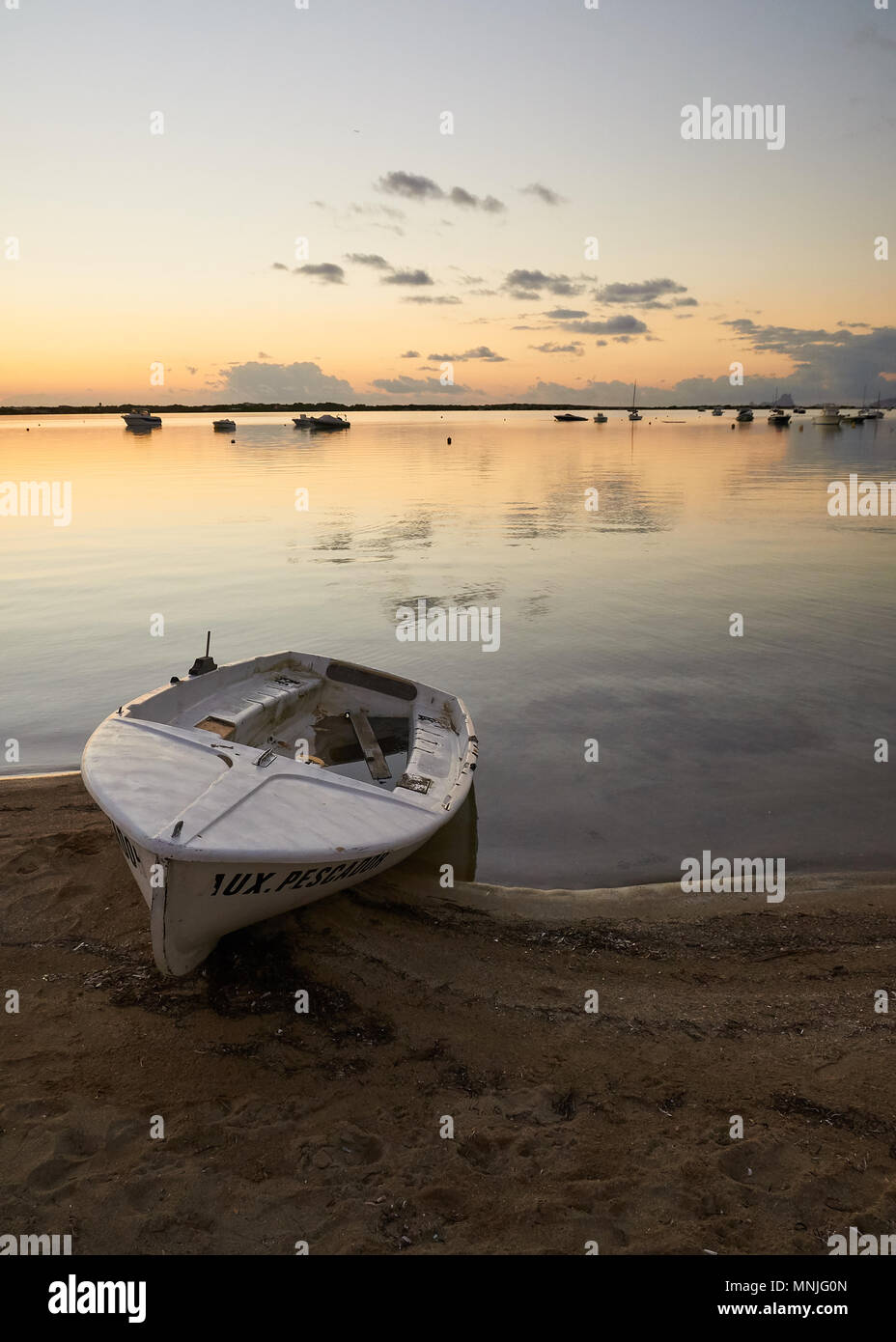 Beached skiff at sunset with anchored sailing boats and clouds reflection at Estany des Peix lagoon in La Savina (Formentera, Balearic Islands, Spain) Stock Photo