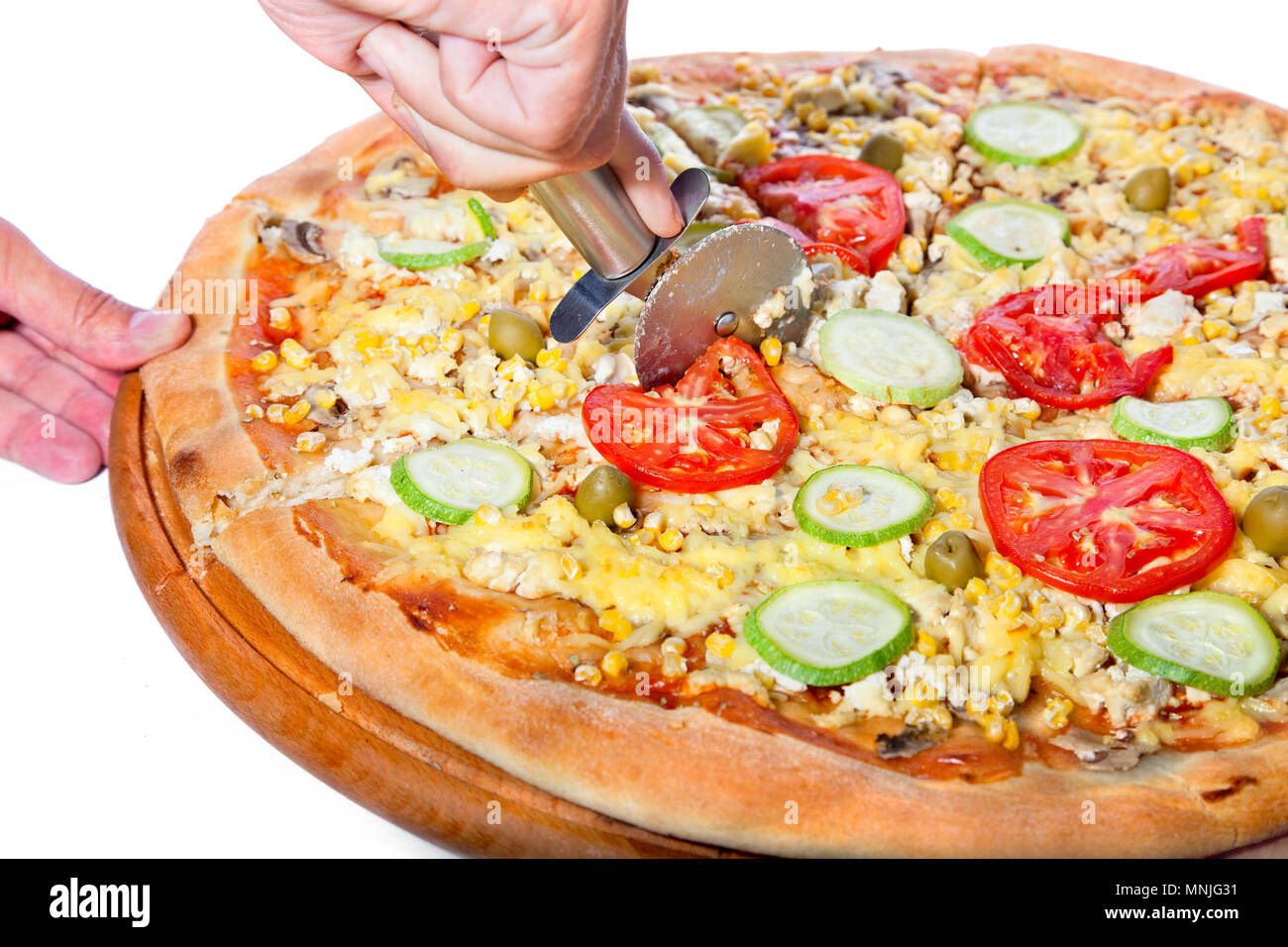 Cutting a tasty vegetable pizza in slices. Pizza made from soya cheese, tomato, ketchup, corn, marrow, mushroom, olives Stock Photo