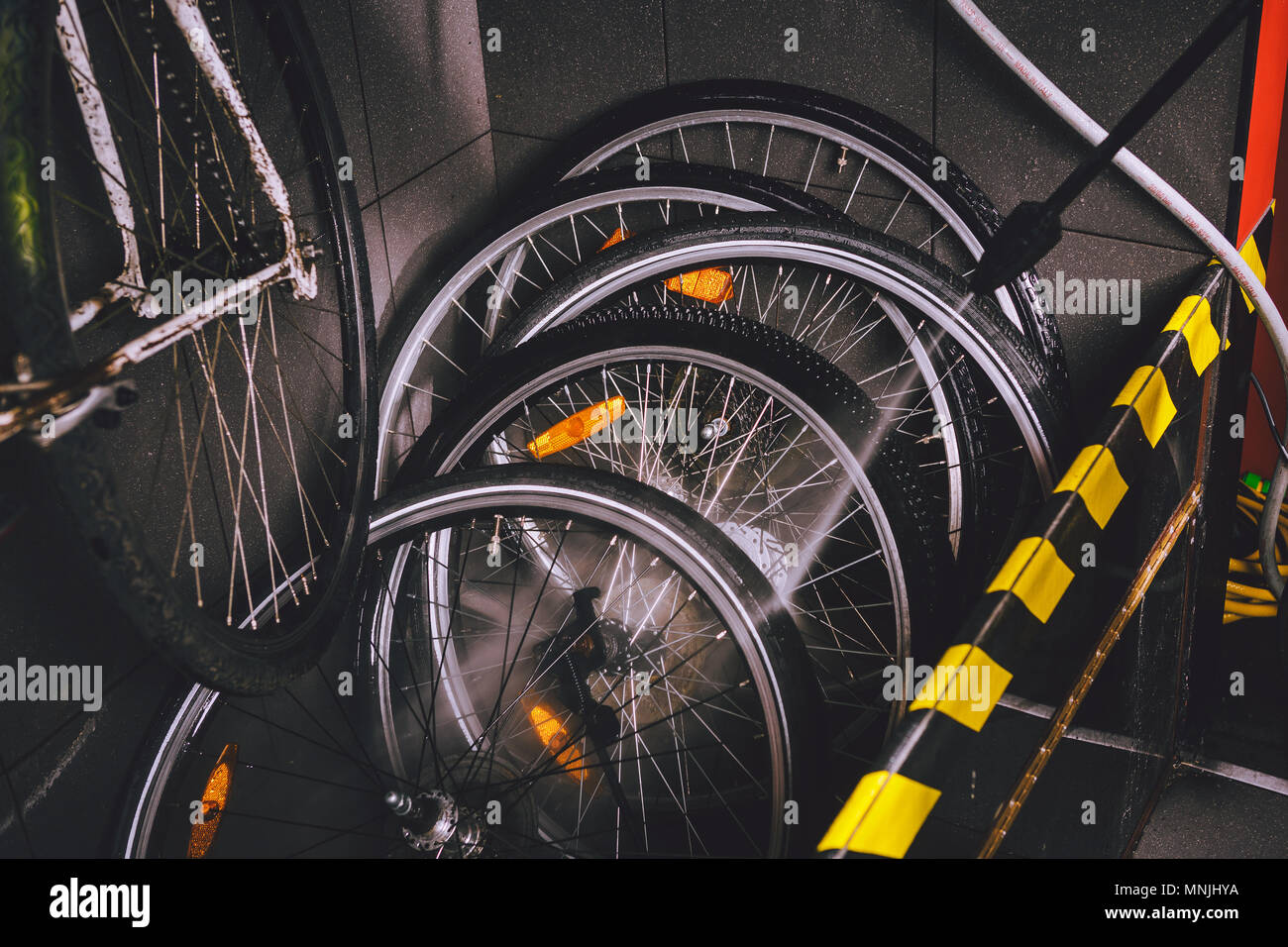 Services professional washing of bicycle in the workshop. Close-up of hand Young Caucasian stylish man doing bicycle cleaning using an automatic electric water pump. Sprays scatter from the pressure Stock Photo