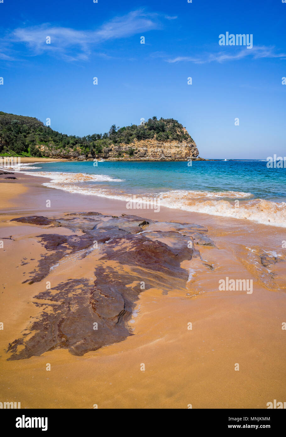 rocky outcrop on the beach at Maitland Bay against the backdrop of the Bouddi Point headland, Bouddi National Park, Central Coast, New South Wales, Au Stock Photo