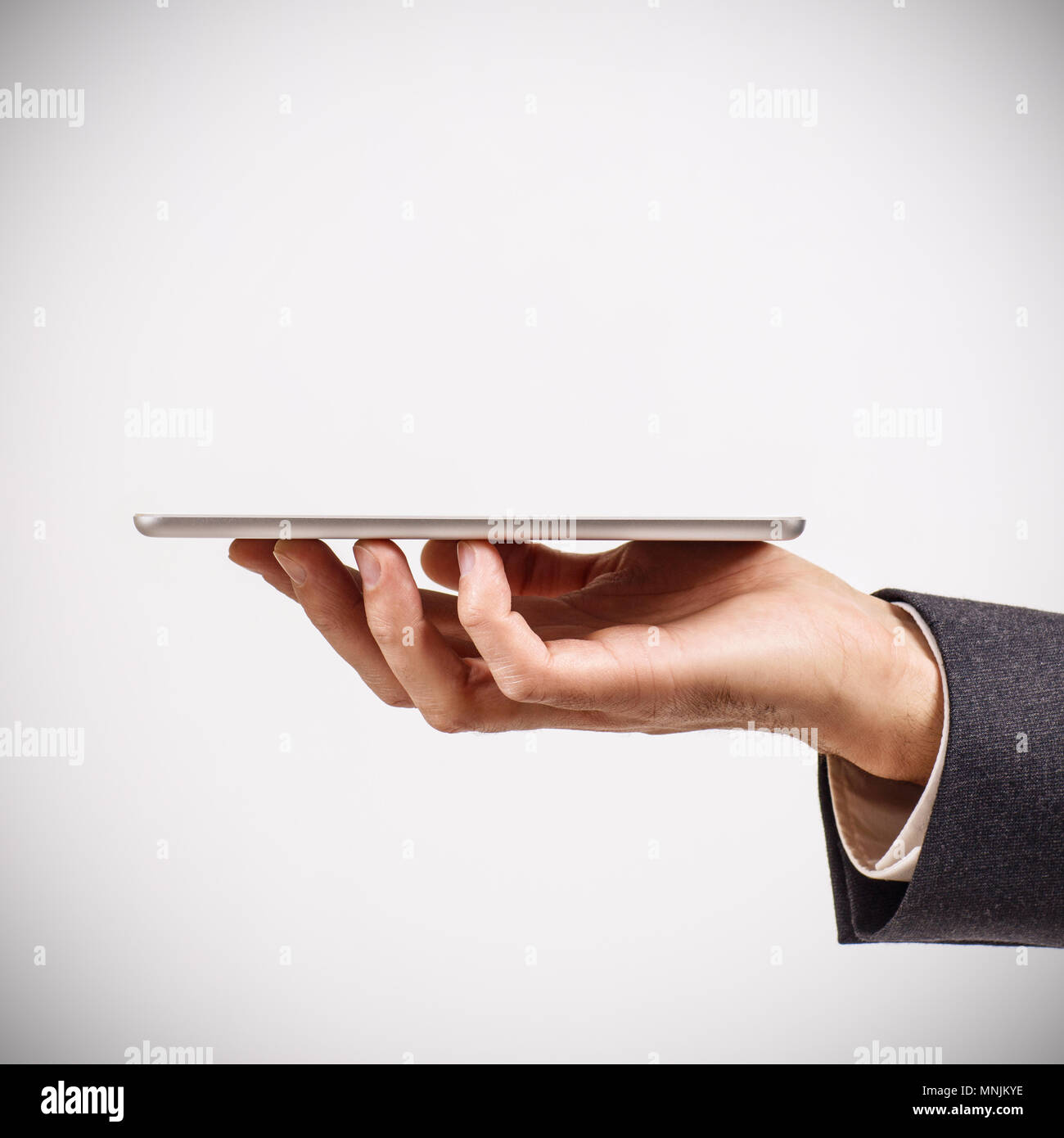 Businessman holds digital tablet against gray background. Stock Photo