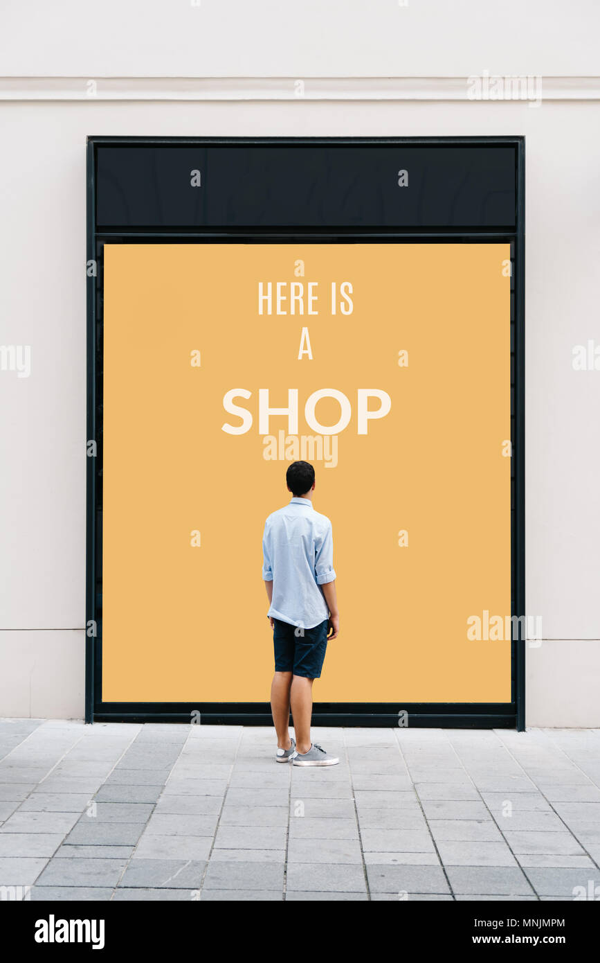 Young man from behind in front of store showcase with text: Here is a ...