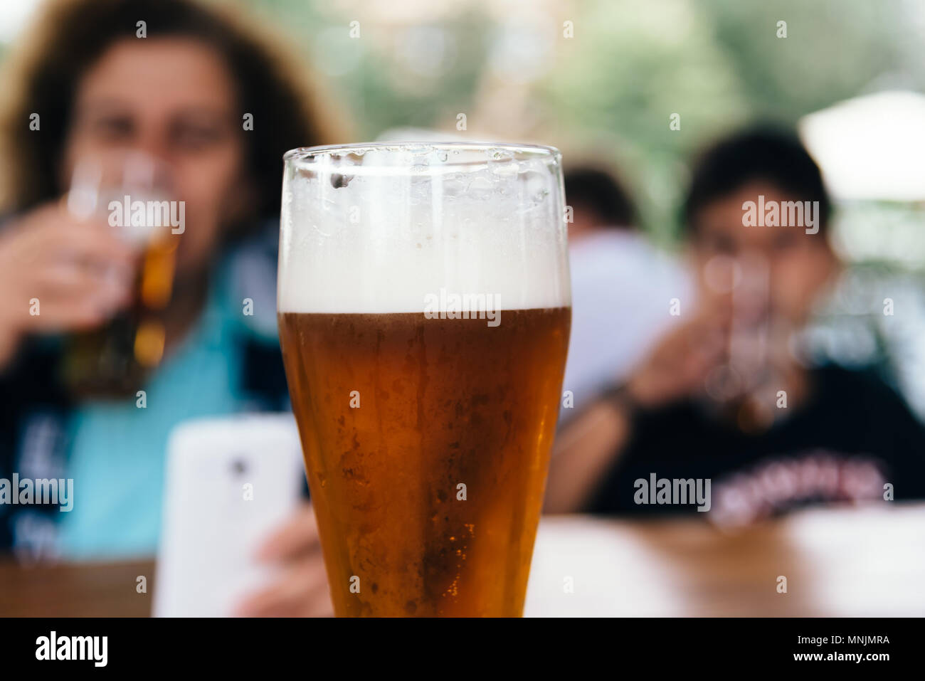 Close up of refreshing pint of lager beer against family in bar. Selective focus Stock Photo