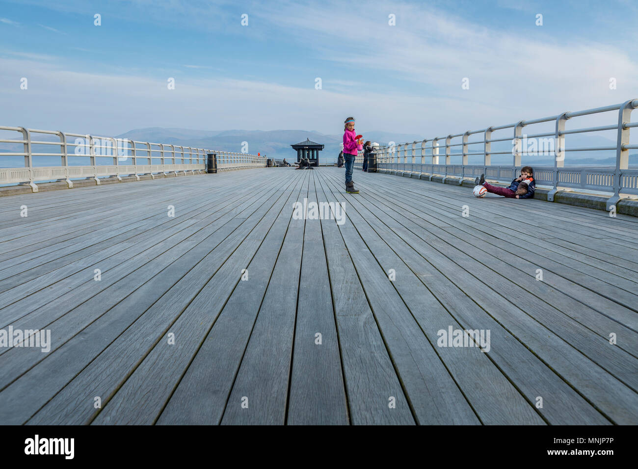 Tourists enjoying a sunny spring evening on a wooden pier with views of Snowdonia mountains, Beaumaris Pier, Anglesey, North Wales, UK Stock Photo
