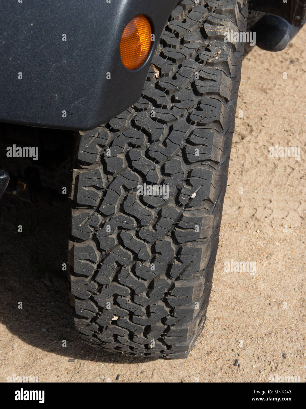 An aggressive offroad tire mounted on a Jeep sitting in the sand Stock