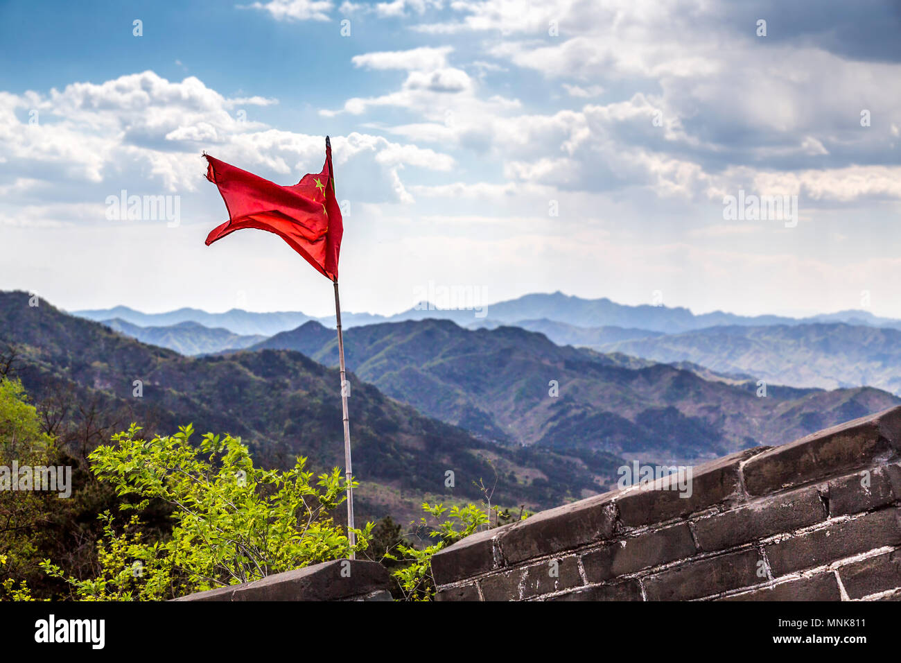 View from The Great Wall Of China at Mutianyu. A Chinese flag blowing in the wind and mountainous terrain stretching as far as the eye can see. Stock Photo