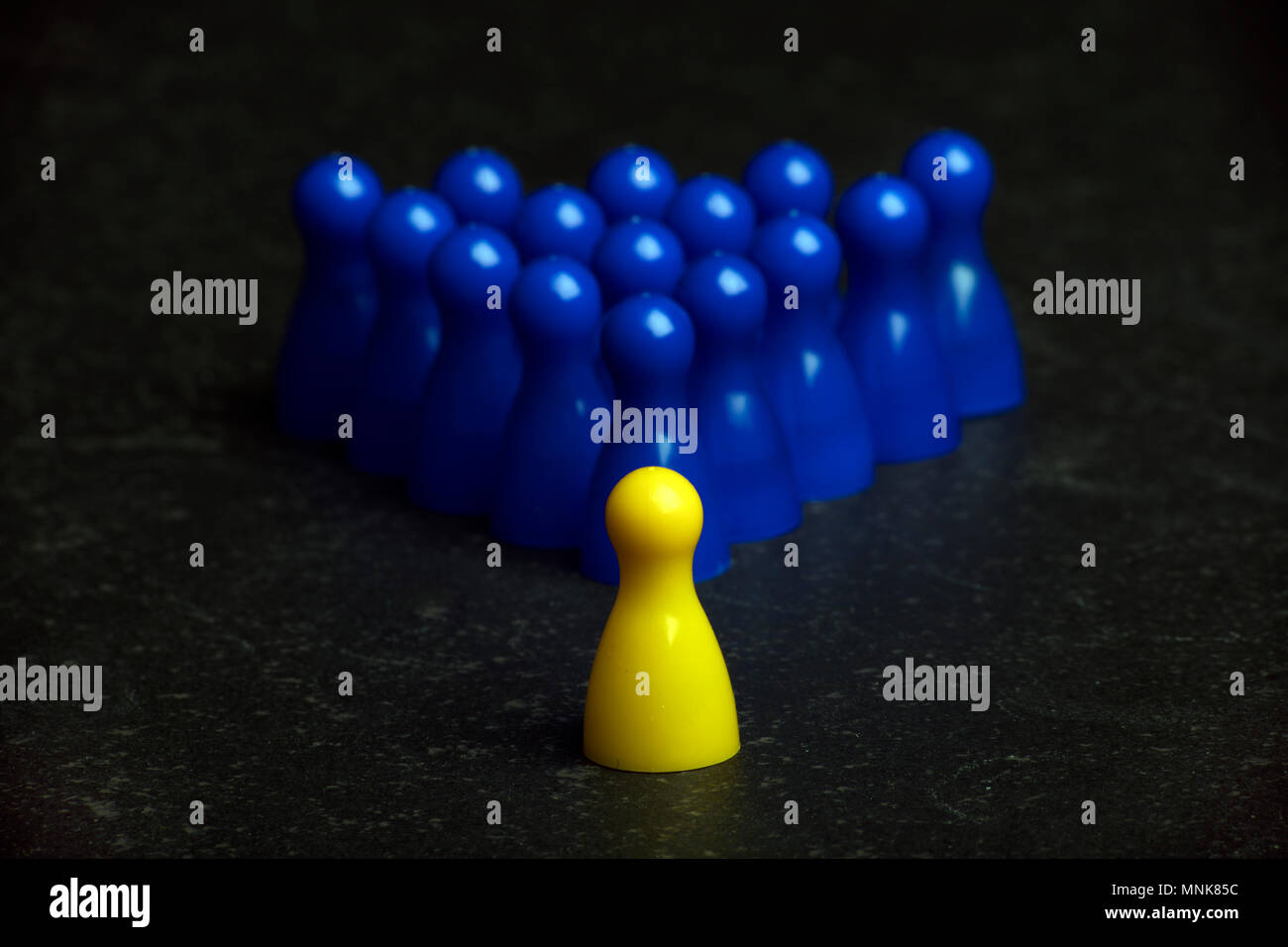 one yellow pawn and a group of blue pawns on a table Stock Photo