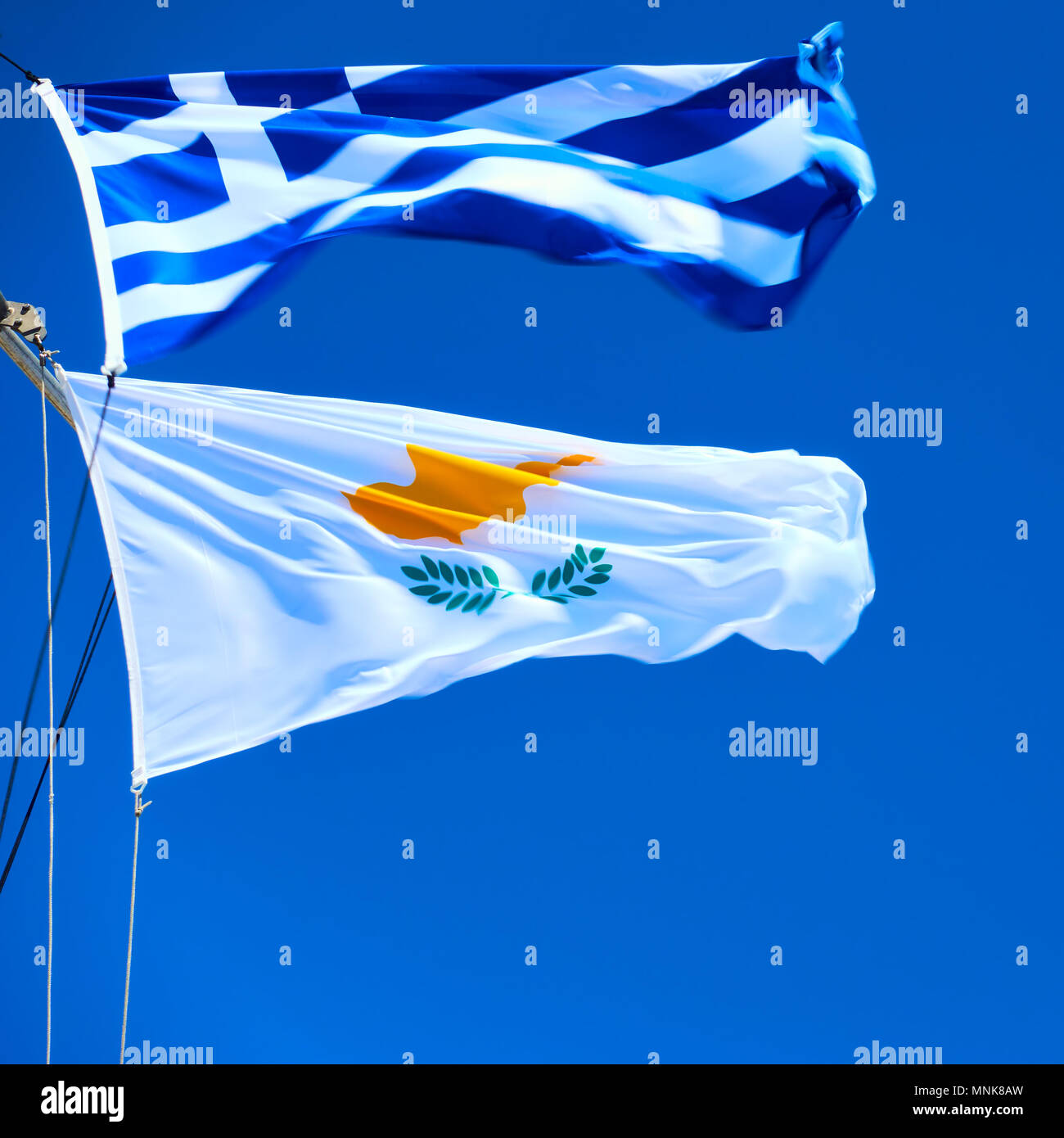 Waving Greek and Cyprian flags agaist the blue sky in strong wind Stock Photo