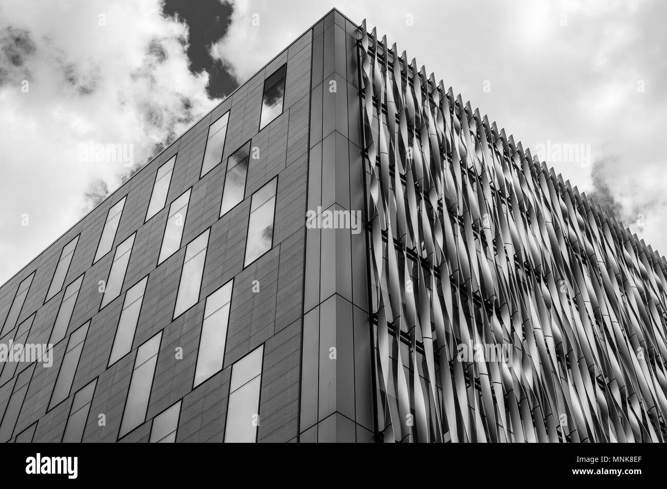 A black and white image looking up at a modern city office building against a cloudy sky in London Stock Photo