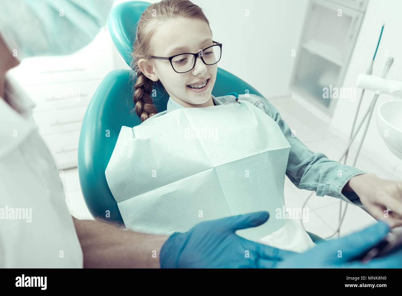 Curious girl with braces on her teeth sitting in a dental chair Stock Photo