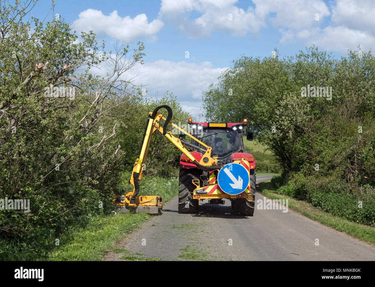 Grass verges being cut by large tractor mower in Sussex country lane during Springtime. Stock Photo