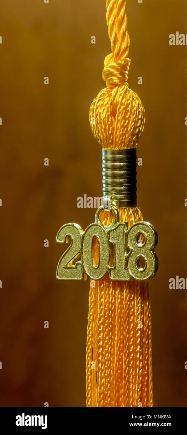 Class of 2018. Gold tassel drop graduation gown accessory and keepsake against a brown background. Iconic symbol of academic achievement. Stock Photo